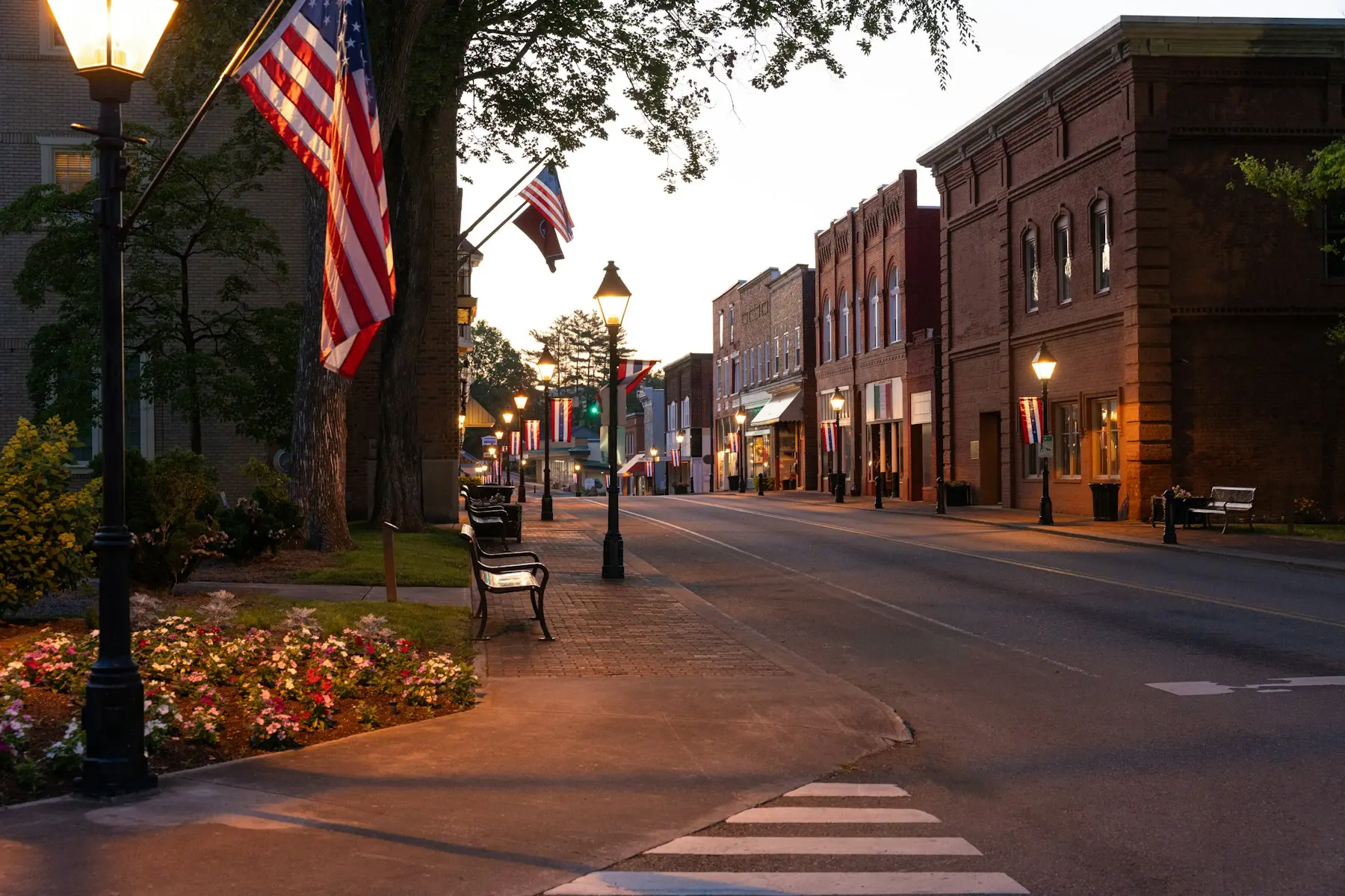 A small-town main street at dusk, lined with American flags and brick storefronts.