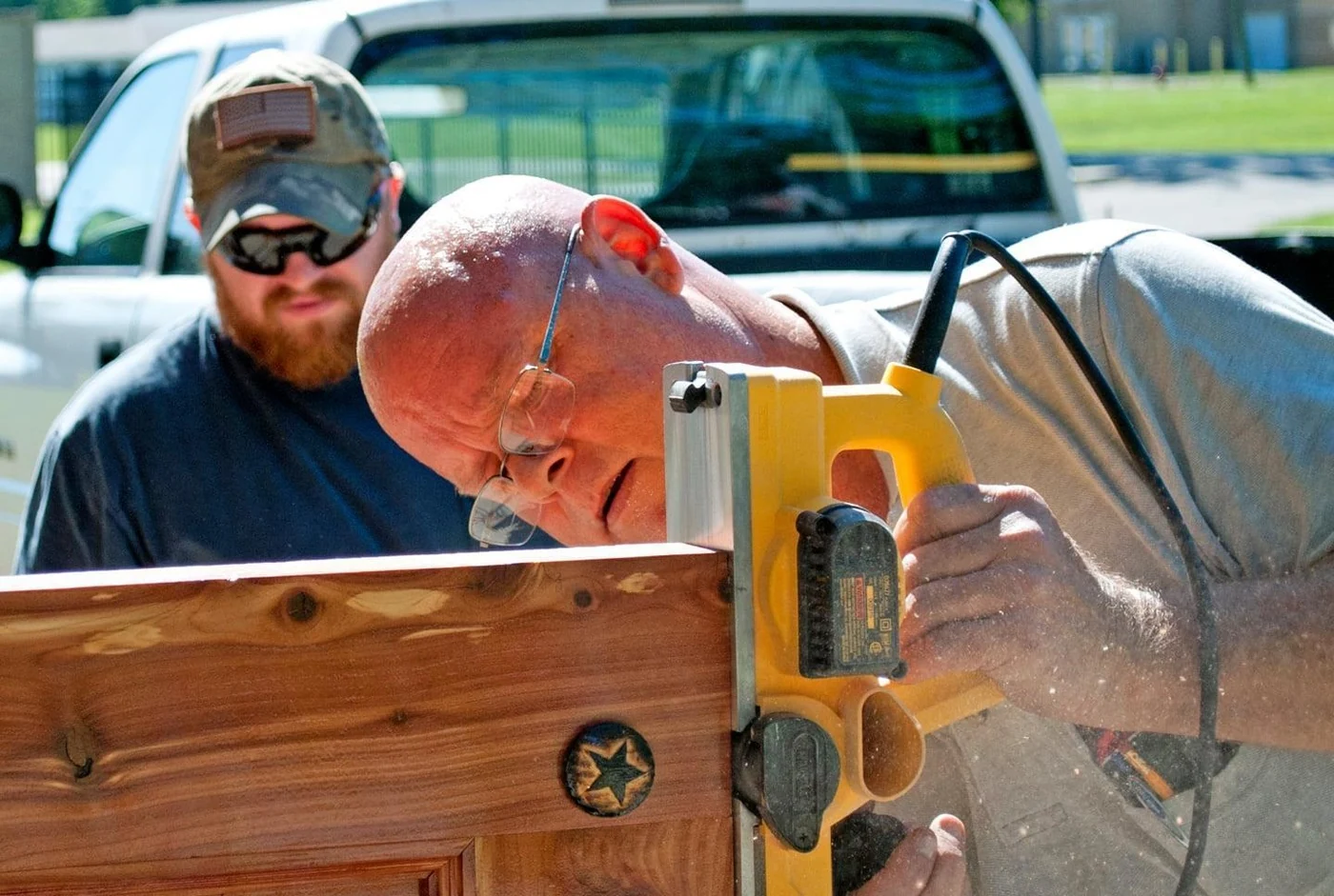 State carpenter Shawn Kostek planes a replacement door at Muscatatuck Urban Training Center in Indiana while Darby Morris observes, July 2020.