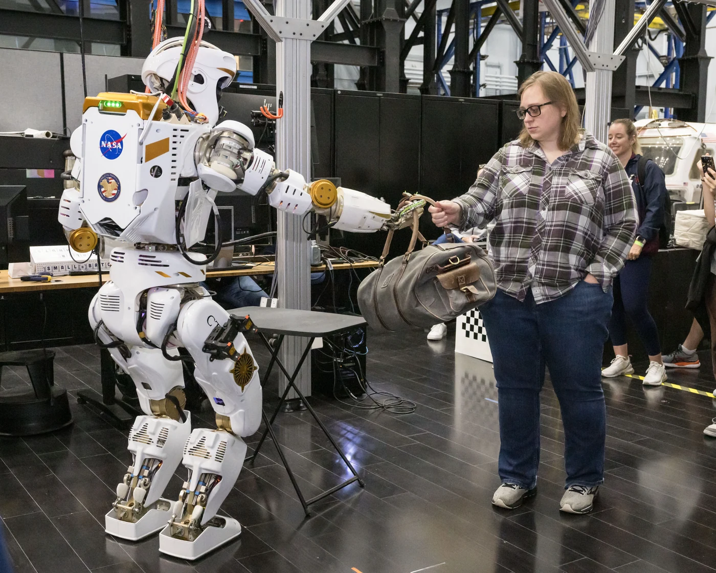 NASA Dexterous Robotics Team member Emma Zemler receives a duffel bag from Valkyrie during a robot demonstration at Johnson Space Center.